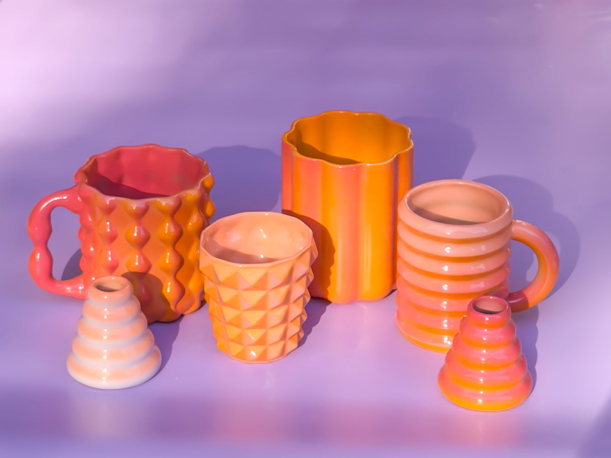 Collection of colorful ceramic mugs and vases on a purple background