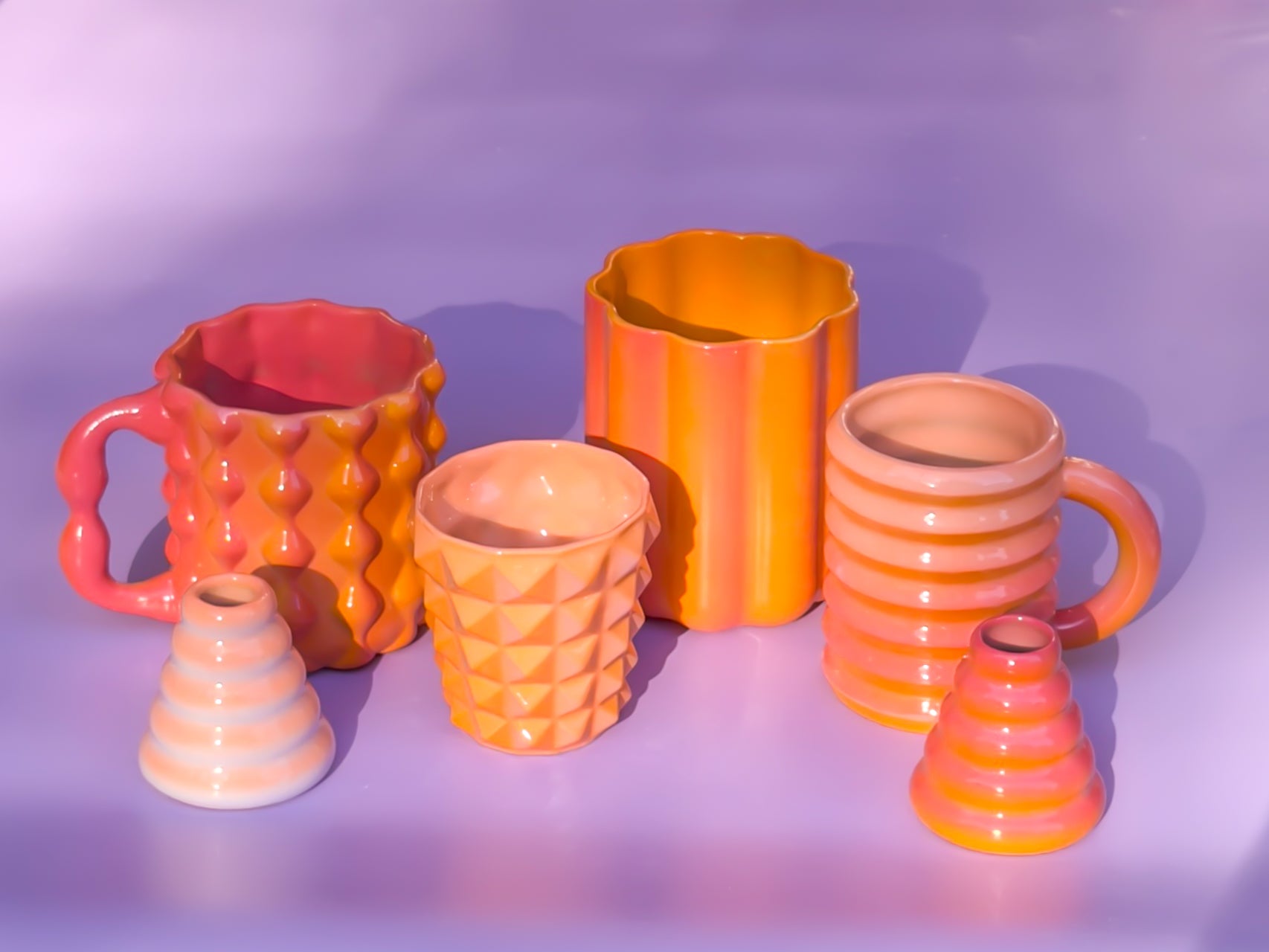 Collection of colorful ceramic mugs and vases on a purple background